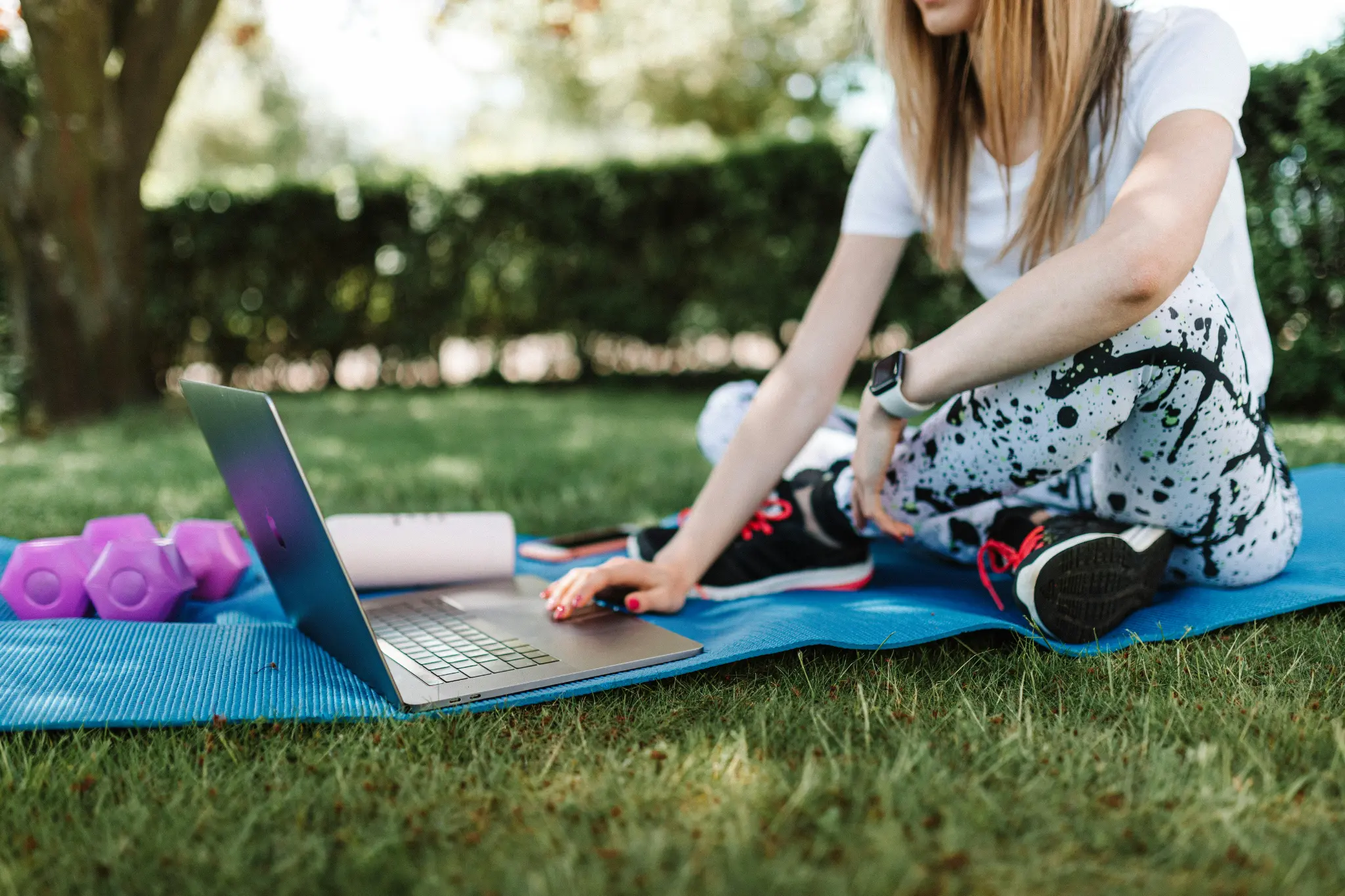 Woman training outdoors on grass with laptop for virtual coaching